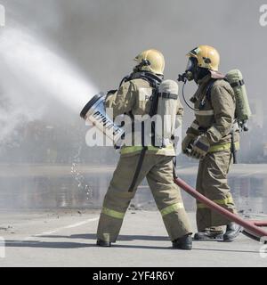 Zwei Feuerwehrleute löschen das Feuer aus dem Löschschlauch, indem sie Wasser-Schaumstoff-Fass mit luftmechanischem Schaum verwenden. Professioneller Urlaub Feuerwehrleute Da Stockfoto