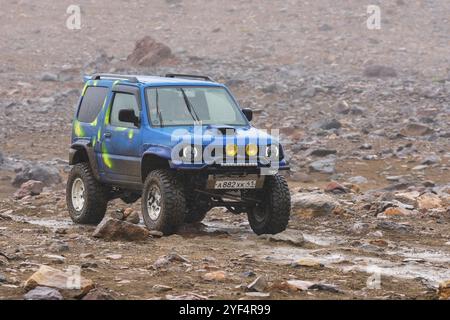 Japanischer SUV Suzuki Jimny Fahren auf felsigen Mount Road auf Hintergrund vulkanischen Landschaft. Aktivurlaub, Reiseziele, Offroad-Reise in regnerischen w Stockfoto