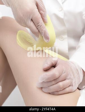 Nahaufnahme von Kosmetikerhändern, die Frauenbeine mit grünem heißem Wachs im Schönheitssalon enthaeben. Teil der Fotoserie Stockfoto