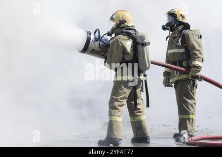 Zwei Feuerwehrleute löschen das Feuer aus dem Löschschlauch, wobei sie Wasser-Schaumstofffass mit luftmechanischem Schaum verwenden. Professioneller Urlaub Feuerwehrmann Tag. Stockfoto