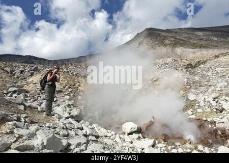 NATURPARK NALYCHEVO, VULKAN DZENZUR, HALBINSEL KAMTSCHATKA, RUSSISCHER FERNOST, 4. SEPTEMBER, 2014: Junge Frau fotografiert dampfende heiße spr Stockfoto