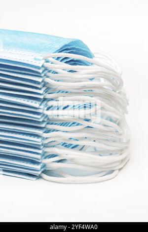 Stapel von blauen medizinischen chirurgischen Gesichtsmasken mit Ohrbändern auf weißem Hintergrund. Konzept Pandemie Versicherung Coronavirus, covid-19. Nahaufnahme erzwungene Persp Stockfoto