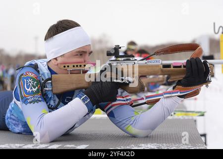 Sportlicher Biathlet, der Gewehrschießen in Bauchlage ausrichtet. Biathlet Andrej Krutov Chanty-Mansijsk auf dem Schießstand. Junior Biathlon Wettbewerbe Ost Stockfoto