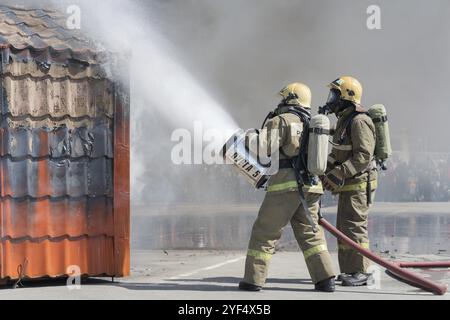 Zwei Feuerwehrleute löschen das Feuer aus dem Löschschlauch, indem sie Wasser-Schaumstoff-Fass mit luftmechanischem Schaum verwenden. Professioneller Urlaub Feuerwehrleute Da Stockfoto