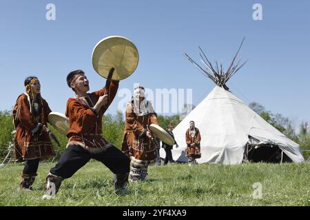 YELIZOVO STADT, KAMTSCHATKA HALBINSEL, RUSSISCHER FERNOST, 15. JUNI 2013: Männer und Frauen tanzen mit einem Tamburin auf dem Gras auf einem Hintergrund Yaranga. Cel Stockfoto