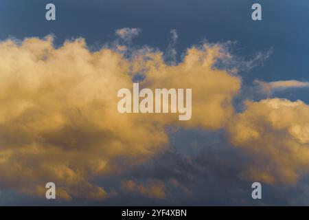 Atemberaubende, flauschige Gewitterwolken, die bei Sonnenuntergang von verschwindenden Strahlen beleuchtet werden, und dunkler Kumulonimbus, der über den sonnigen blauen Himmel schwebt, um die Jahreszeit zu ändern Stockfoto