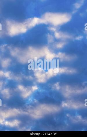 Dramatische Wolken am blauen Himmel, beleuchtet von Sonnenstrahlen bei Sonnenuntergang, um das Wetter zu ändern. Weicher Fokus, Bewegungsunschärfe mehrfarbige Wolkenlandschaft abstrakter Hintergrund Stockfoto