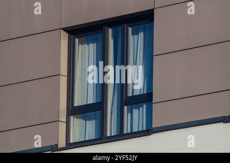 Sonnenlicht beleuchtende Vorhänge hinter einem Fenster eines modernen Wohngebäudes mit brauner Fassade Stockfoto