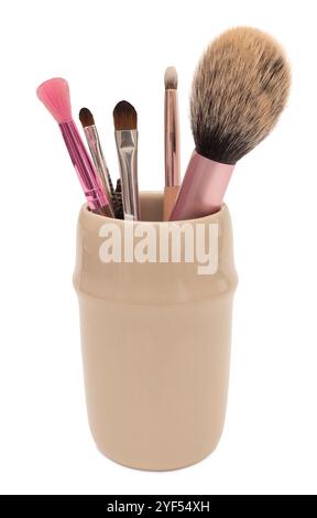 Beigefarbener Keramikhalter gefüllt mit verschiedenen Make-up-Pinseln, einschließlich Puder-, Blending- und Lidschattenpinsel. Isoliert auf weißem Hintergrund, Vorderansicht Stockfoto