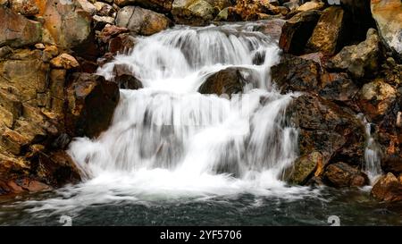 Ein kleiner Wasserfall mit klarem Wasser fließt schnell über große natürliche Felsen und schafft einen bezaubernden und beruhigenden Blick. Stockfoto