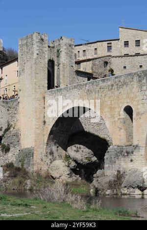 Besalu;Spanien;03302018: Eine historische Steinbrücke mit zwei Türmen, die sich über einen Fluss erstreckt. Die Brücke hat ein Bogendesign und ist von grünem umgeben Stockfoto