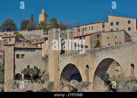 Besalu;Spanien;03302018: Malerischer Blick auf eine mittelalterliche Steinbrücke, die zu einem charmanten Dorf mit Steinhäusern führt, vor einem klaren blauen Himmel. Stockfoto