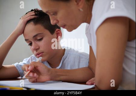 Eine Mutter hilft ihrem Sohn bei Hausaufgaben zu Hause und betont die Bedeutung von Bildung. Der kleine Junge sieht konzentriert und entschlossen aus, während er in s eingreift Stockfoto