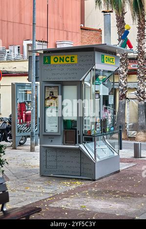 Viladecans. Spanien - 03. November 2024: Straßenblick auf einen EHEMALIGEN Lotterieautomaten mit Braille-Schildern, Glaspaneelen und Werbeplakaten. Der Kiosk ist s Stockfoto