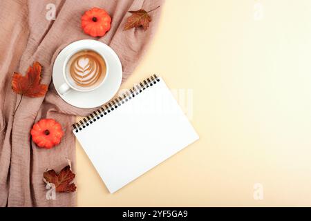 Tasse Kaffee, Kürbisse, Herbstblätter und leerer Notizblock auf aschrosa Tischdecke auf neutralem Hintergrund. Herbst, Herbst, Thanksgiving-Konzept. Bis Stockfoto