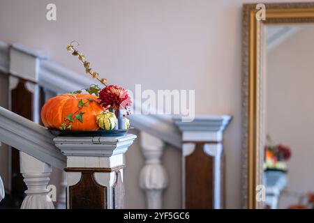 Einfaches Herbstblumenarrangement mit roter Chrysantheme, Efeu und Kürbissen. Inneneinrichtung mit Herbstblumen und Kürbissen auf Holztreppensäule. Stockfoto