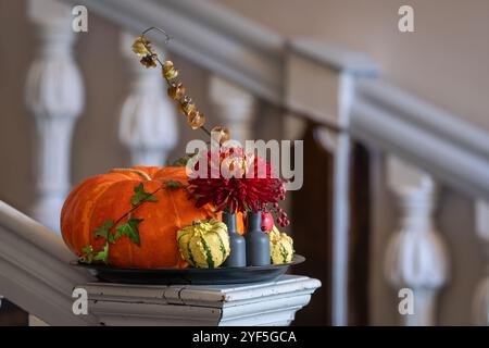 Einfaches Herbstblumenarrangement mit roter Chrysantheme, Efeu und Kürbissen. Inneneinrichtung mit Herbstblumen und Kürbissen auf Holztreppensäule. Stockfoto