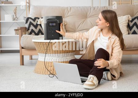 Junge Frau, die zu Hause einen Laptop mit einem tragbaren Kraftwerk auflädt Stockfoto