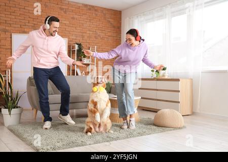 Ein junges Paar in Kopfhörern mit dem australischen Schäferhund, der zu Hause tanzt Stockfoto