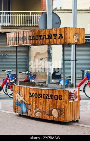 Viladecans. Spanien - 3. November 2024: Traditioneller Holzwagen für den Verkauf von Kastanien und Süßkartoffeln, auf einer städtischen Straße mit Fahrrädern ne Stockfoto