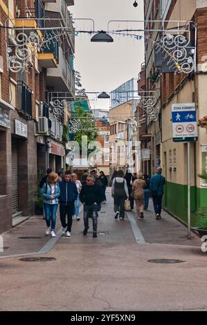 Viladecans. Spanien - 03. November 2024: Urbane Szene in Viladecans mit einer Fußgängerzone mit dekorativen Lichtern, lokalen Geschäften und Menschen, die spazieren gehen, i Stockfoto