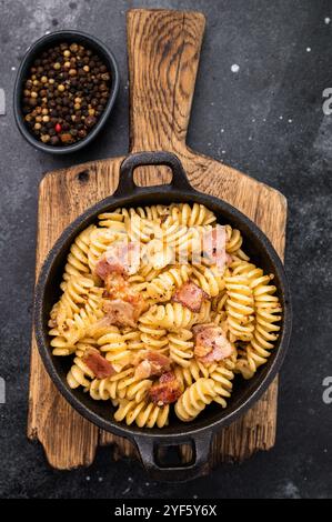 Fusilli Carbonara Nudeln mit knusprigen Speckstückchen und Parmesankäse in einer Pfanne. Schwarzer Hintergrund. Draufsicht. Stockfoto