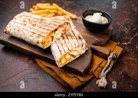 Shawarma-Hähnchenbrötchen mit frischem Gemüse, Cremesauce und Pommes frites auf Holzbrett. Brauner Hintergrund. Draufsicht. Stockfoto