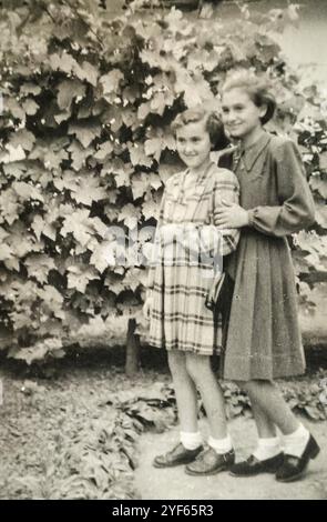 Jugoslawien - 1950er Jahre: Zwei lächelnde junge Mädchen posieren in einem Garten vor dem Weinstock Stockfoto