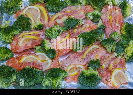 Nahaufnahme von rohen Lachsfilets mit Zitronenscheiben und Brokkoli-Röschen auf Folie, zubereitet zum Backen. Stockfoto