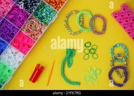 Bunte Webarmbänder Armbänder, Box mit mehrfarbigen Gummibändern und andere Armbänder, die Vorräte auf gelbem Hintergrund machen. Stockfoto