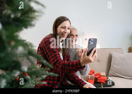 Feiern Sie Weihnachten, Silvester, Mutter und Tochter halten ein Smartphone-Selfie und machen Sie Fotos, grüßen Sie während der sozialen Distanz per Videoanruf Stockfoto