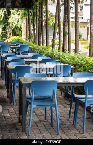 Café im Freien mit Holztischen und Hockern in einer Stadtstraße. An einem sonnigen Sommertag stehen Holztische und blaue Stühle in einem Café im Freien. Ein gemütliches Outdoo Stockfoto