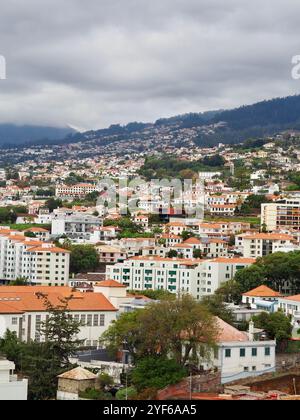 Eine faszinierende Aussicht umfasst moderne Hochhäuser in Kombination mit traditionellen Strukturen, die über eine hügelige Stadtlandschaft verstreut sind, unter einem bewölkten Himmel, die Sie zeigen Stockfoto