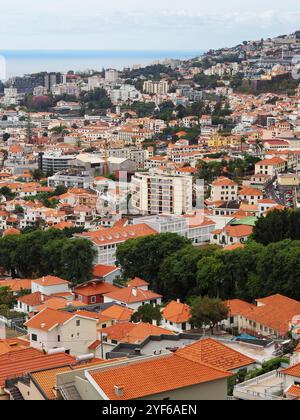 Eine faszinierende Aussicht umfasst moderne Hochhäuser in Kombination mit traditionellen Strukturen, die über eine hügelige Stadtlandschaft verstreut sind, unter einem bewölkten Himmel, die Sie zeigen Stockfoto