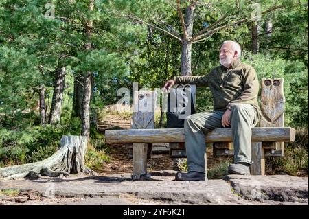 Ein älterer Wanderer sitzt auf Eulenfelsen im Pfälzerwald. Mit der Sonne im Gesicht genießt er die weite Sicht von. Stockfoto