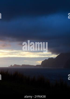 Ein atemberaubender Sonnenuntergang über dem Meer mit dunklen, dramatischen Wolken und zerklüfteten Klippen, die eine kraftvolle, stimmungsvolle Szene voller Kontraste und natürlicher schönheit schaffen Stockfoto