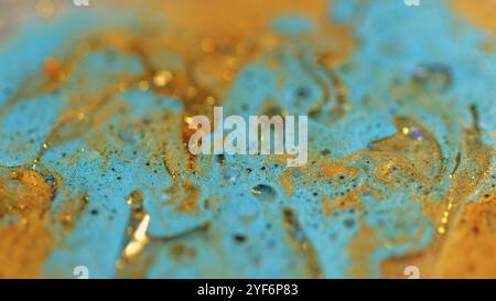 Verschütteter flüssiger Glitzer. Glänzende Tinte. Unschärfe blau goldene Farbe metallische Pailletten Partikel Glanz Blasen flüssige Farbe Mischung abstrakte Kunst Hintergrund mit Bokeh Lichter. Stockfoto