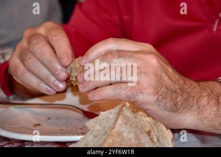 Nahaufnahme der Hände eines Mannes, der ein Stück rustikales Brot hält. Perfekt für Themen wie Tradition, Essen, Einfachheit und Handwerkskunst Stockfoto