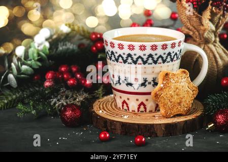 Kaffeetasse mit Weihnachtsmotiv und einem Keks, weihnachtsdekoration und weihnachtsbeleuchtung auf einem grauen Tisch. Hintergrund des Weihnachtskonzepts Stockfoto