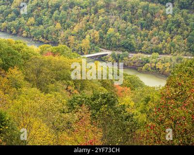 Im New River Gorge National Park umgeben Berge, die von Frühherbstlaub bedeckt sind, Brücken, die den Fluss überqueren, und schaffen so eine malerische Herbstlandschaft. Stockfoto