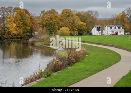 Ein Flussweg entlang des Flusses Aire im Roberts Park Saltaire (Baildon) in Yorkshire. Saltaire Cricket Clubhouse ist im Hintergrund. Stockfoto