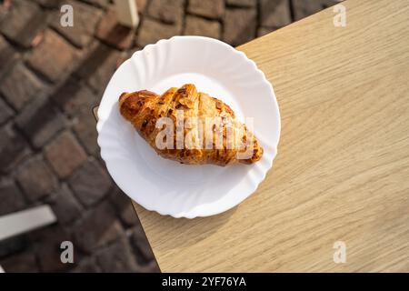 Blick von oben auf ein frisch gebackenes Mandelcroissant auf einem Teller im Freien Stockfoto