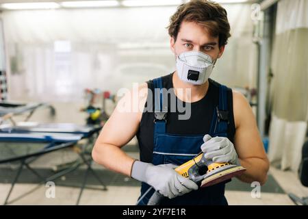 Mechaniker, der Maschinen benutzt, Autopolierer, um Markierungen zu entfernen Reparatur. Porträt eines muskulösen Autolacktechnikers bei Gesichtsmaskenhaltung Stockfoto