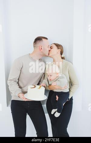 Lächelnde Mutter und Vater halten ein Kind und einen Urlaubskuchen. Eltern, Mom und Dad und lächelndes Baby in den Armen isoliert über weißem Hintergrund. Fröhlich, jung Stockfoto