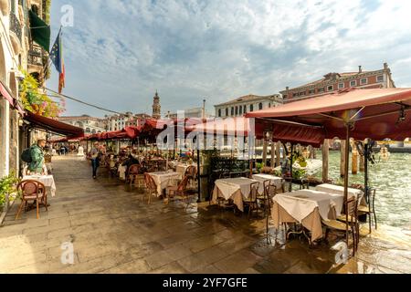 Venedig, Vento – IT – 14. Oktober 2024 Ein charmantes Café am Kanal in Venedig mit roten Markisen, weißen Tischdecken und einem malerischen Blick auf historische Gebäude und Stockfoto