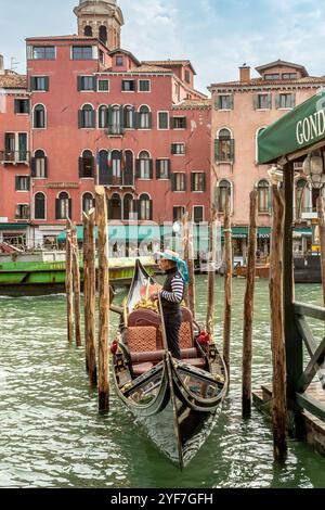 Venedig, Vento – IT – 14. Oktober 2024 Ein Gondoliere steht in einer eleganten, verzierten Gondelbahn, die entlang des Canal Grande in Venedig angedockt wird. Hohe hölzerne Anlegestelle po Stockfoto