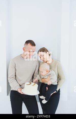 Lächelnde Mutter und Vater halten ein Kind und einen Urlaubskuchen. Eltern, Mom und Dad und lächelndes Baby in den Armen isoliert über weißem Hintergrund. Fröhlich, jung Stockfoto