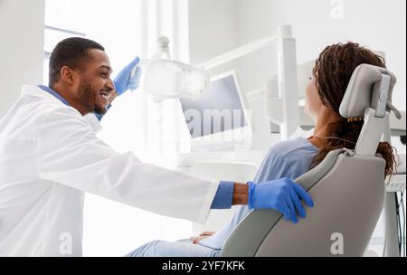 Fröhlicher Zahnarzt im Gespräch mit Frau im Zahnarztstuhl sitzen Stockfoto