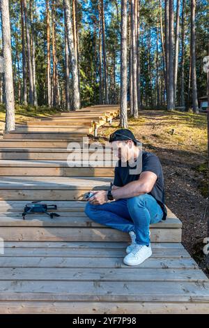 Ein Mann sitzt auf einer Holztreppe in einem Wald, umgeben von hohen Kiefern. Sonnenlicht filtert durch und erzeugt Muster aus Licht und Schatten. Stockfoto