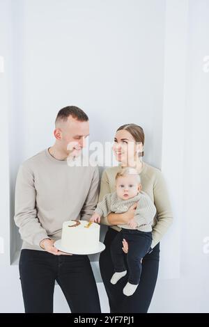 Lächelnde Mutter und Vater halten ein Kind und einen Urlaubskuchen. Eltern, Mom und Dad und lächelndes Baby in den Armen isoliert über weißem Hintergrund. Fröhlich, jung Stockfoto